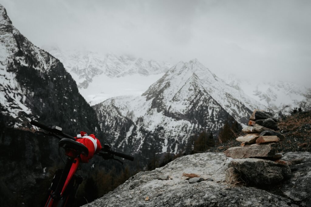 A stunning winter mountain scene featuring a bicycle and a rock cairn with snowy peaks.
