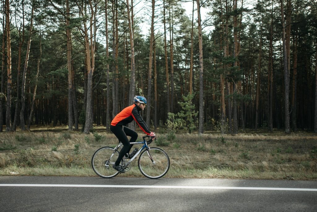 A cyclist in vibrant gear rides a road bike through a serene forest setting.