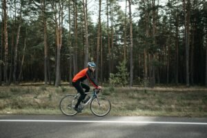 A cyclist in vibrant gear rides a road bike through a serene forest setting.