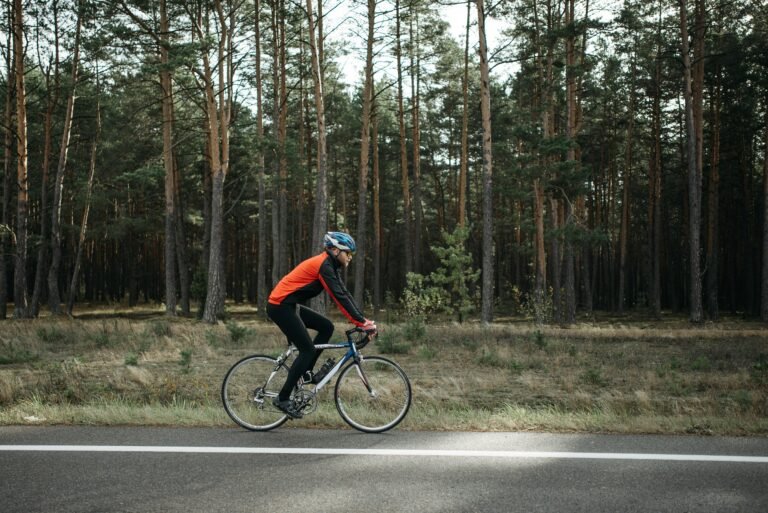 A cyclist in vibrant gear rides a road bike through a serene forest setting.